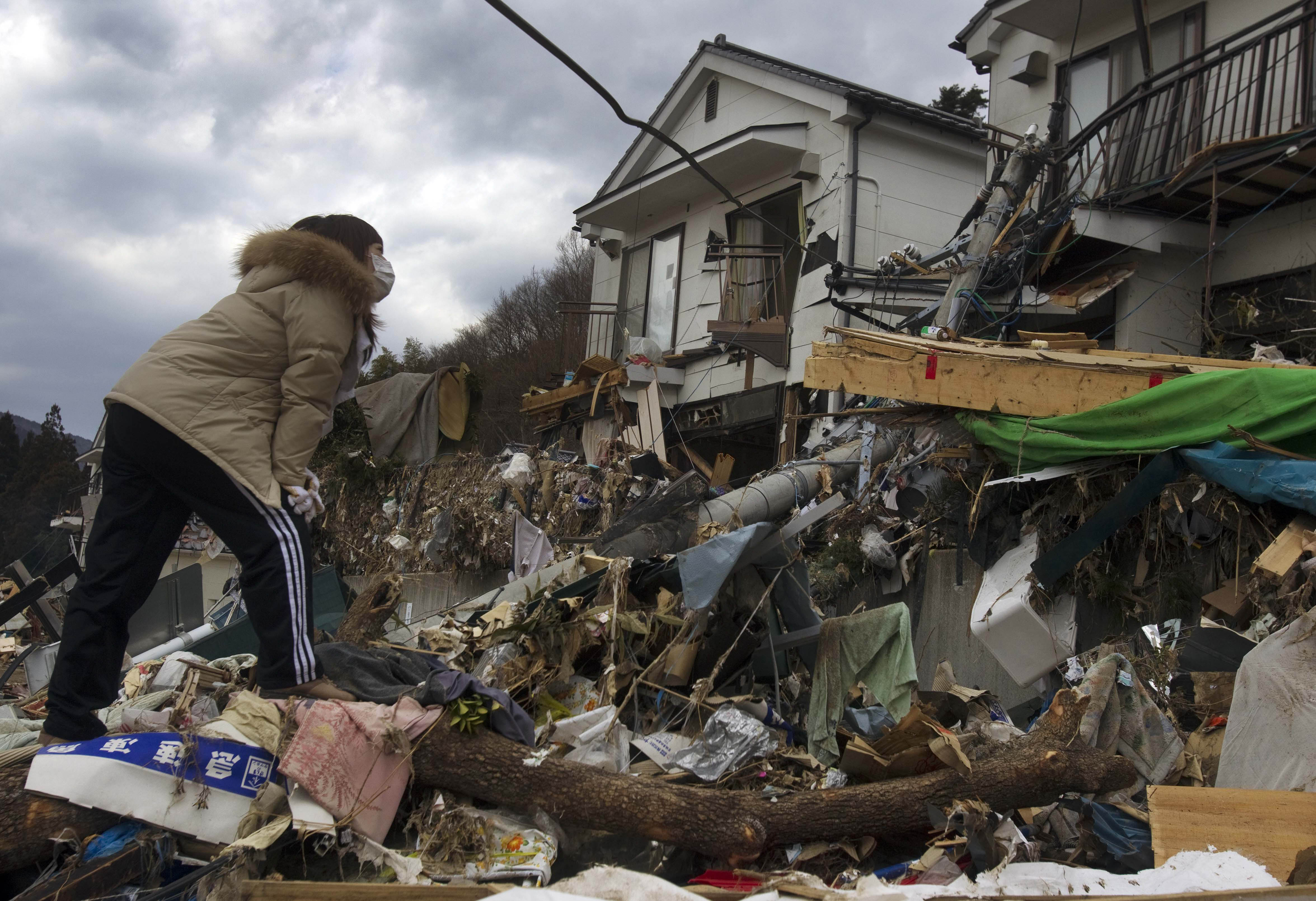Tayo Kitamura, 40, stands on the rubble of the home of her mother, Kuniko Kitamura, 69, as Japanese fireman discover her mother's body in Onagawa, northeastern Japan Saturday, March 19, 2011. (AP Photo/David Guttenfelder)
