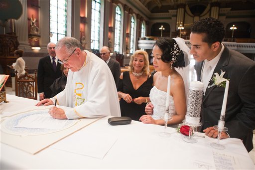 this 2010 image released by Ryan DeVera Photography, Father Kevin Moley, C.Ss.R., left, signs the wedding ketubah of Jannine and Nelson Malavé at St. Peter the Apostle Church in Philadelphia. More non-Jewish couples have embraced Jewish marriage rituals over the last decade. Some stomp a glass _ or a lightbulb as a popular substitute. Others recite vows under a canopy, called a chuppah. But it's the ketubah, or a less Jewish cousin called a "Statement of Our Love," that often catches the eye of couples with no family or cultural ties to Judaism. (AP Photo/Ryan DeVera Photography)